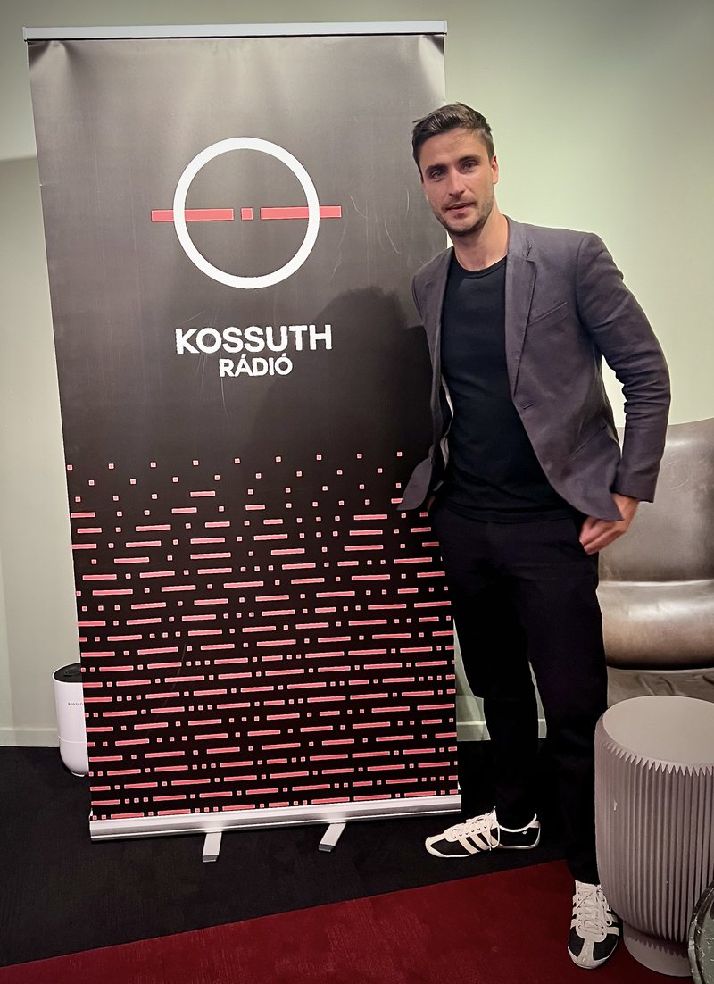 Schmidt Gergő a Kossuth Rádió stúdiójában, a rádió logós molinója mellett